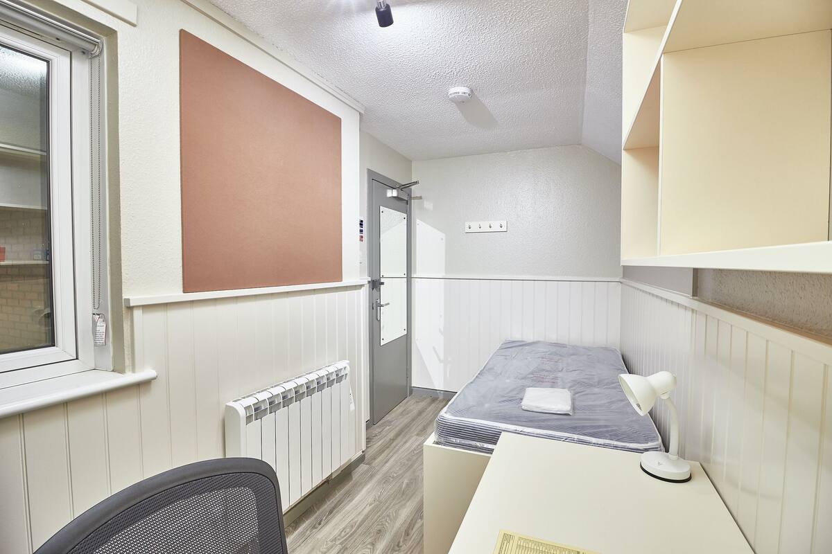 Ein kleines Zimmer mit einem Bett, einem Schreibtisch und einem Stuhl.