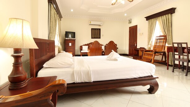 Habitación de hotel con una cama grande, muebles de madera, un escritorio y un ventilador de techo.