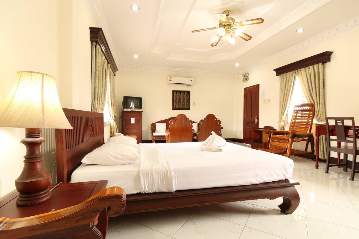 A hotel room with a large bed, wooden furniture, a desk, and a ceiling fan.