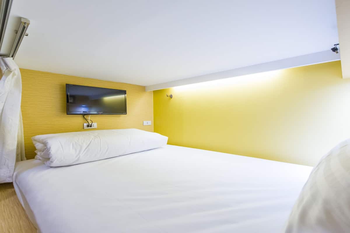 Habitación de hotel con cama, televisor de pantalla plana en la pared y ventana con cortinas.