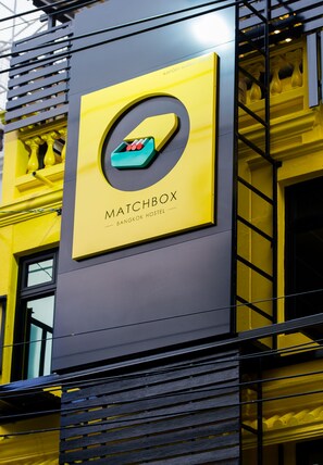 A yellow and black building with a sign for Matchbox Bangkok Hostel.