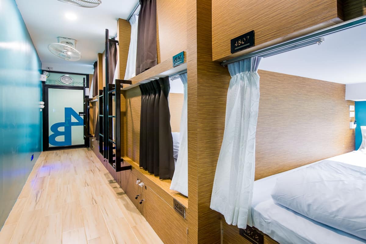 Un pasillo estrecho con paredes y suelo de madera, que conduce a una habitación con cama y ventana con cortinas.