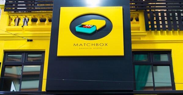 A yellow and black building with a sign that reads "MATCHBOX BANGKOK HOSTEL".