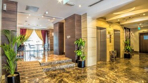 Un vestíbulo de hotel con suelo de mármol, plantas en macetas, un mostrador de recepción y un ascensor.