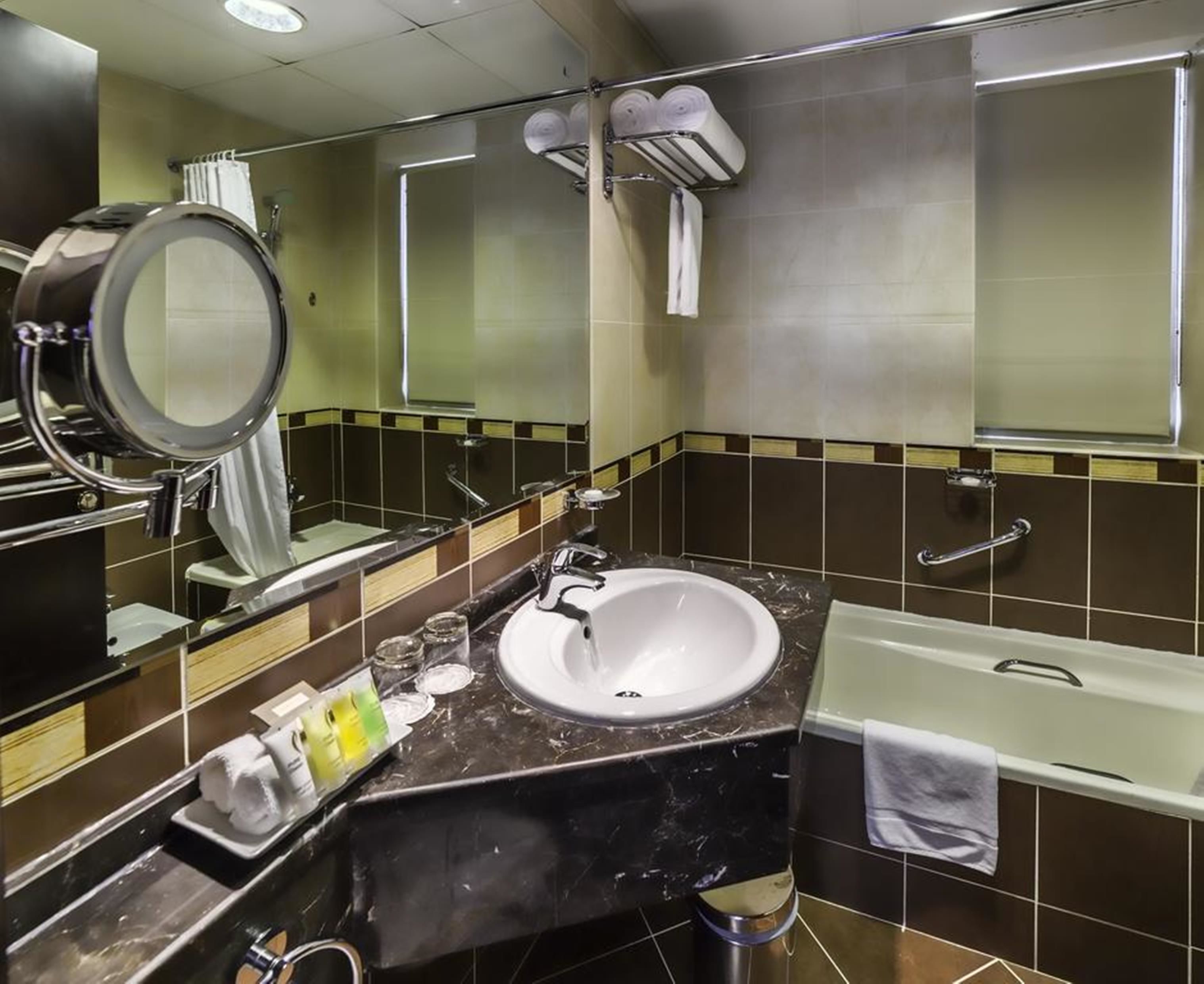 A modern bathroom with a white sink, a large mirror, a bathtub, and a towel rack.
