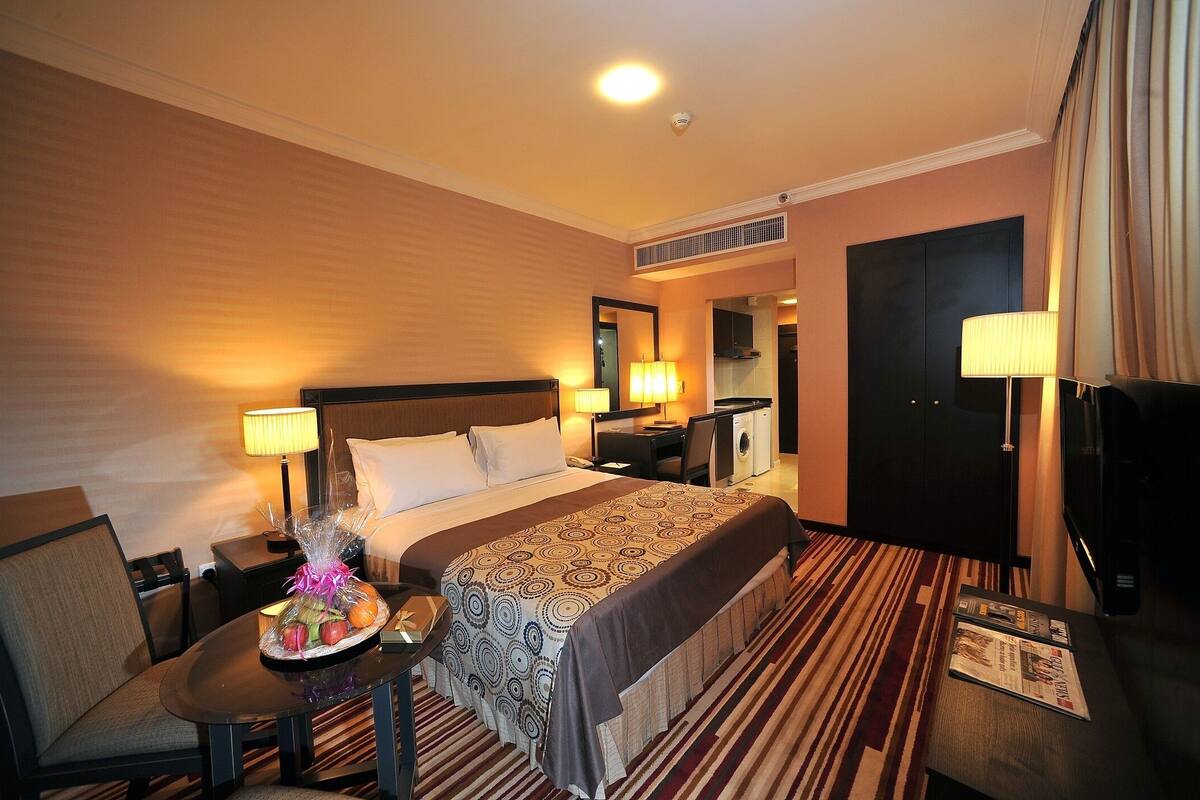 A hotel room with a large bed, bedside lamps, a desk with a lamp, a chair, a TV, and a window with curtains.