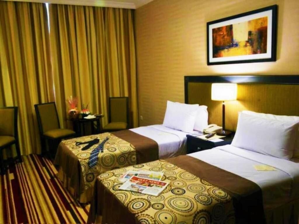 Una habitación de hotel con dos camas, alfombra a rayas, un cuadro en la pared y una mesita de noche con una lámpara.