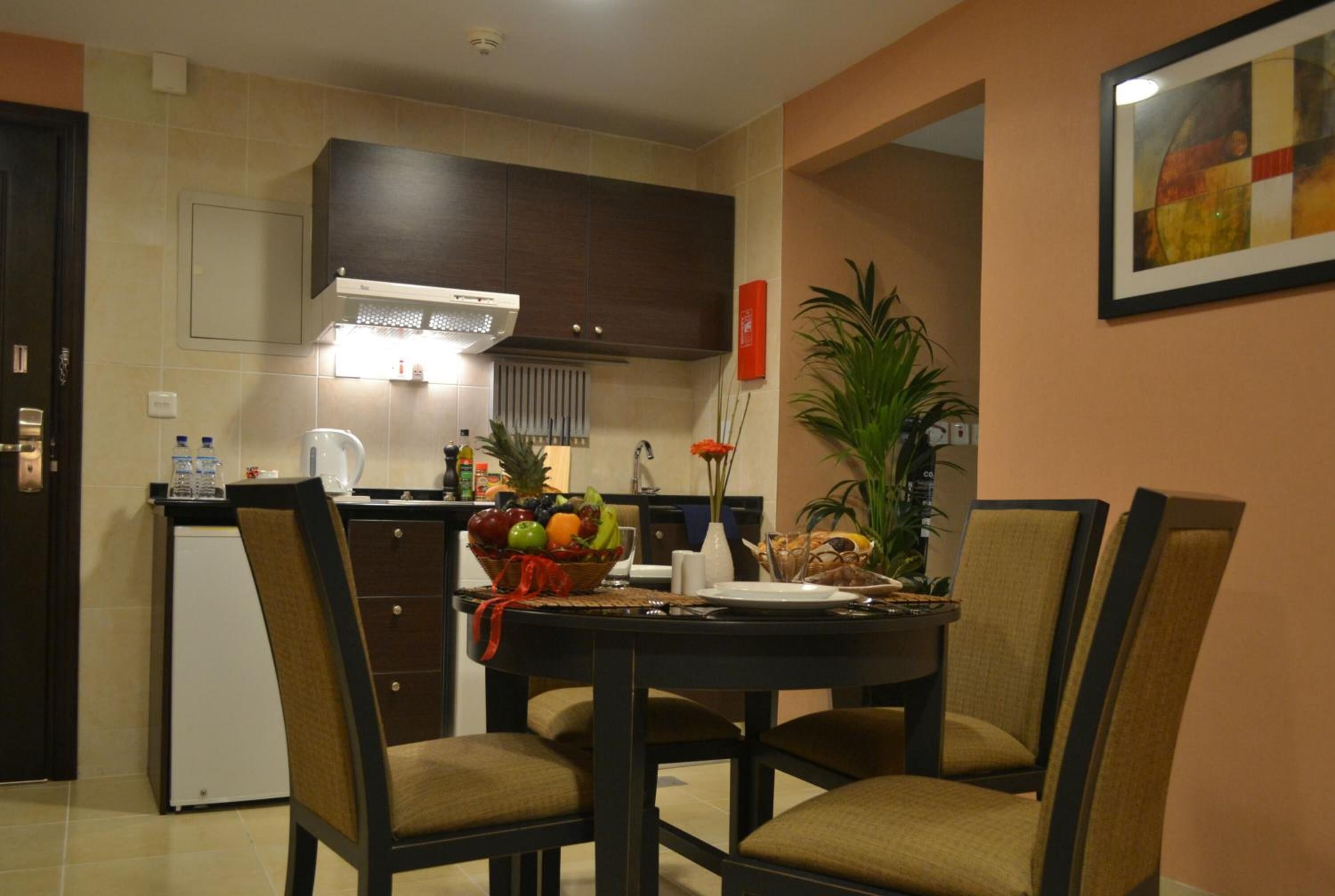 A compact kitchen with dark cabinets, a small refrigerator, and a dining table set for four with chairs.