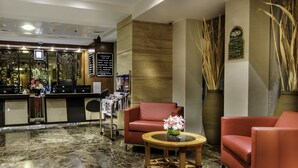 Un hall con mostrador de recepción, asientos de cuero rojo, suelo de mármol y un jarrón decorativo con flores.