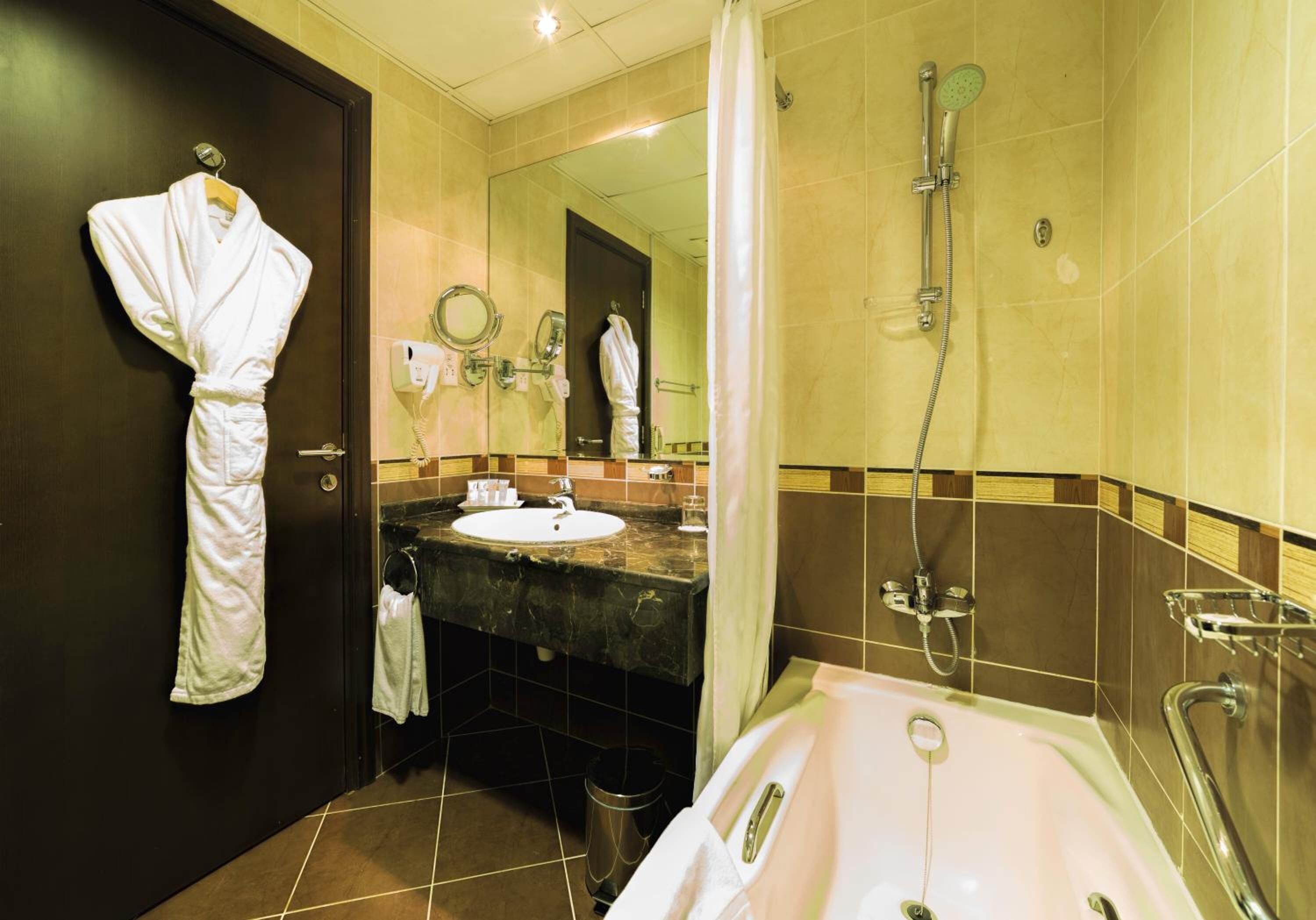Une salle de bain d’hôtel avec une baignoire, un lavabo, un miroir et une robe accrochée au mur.
