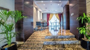 Un moderno vestíbulo de hotel con una escalera de mármol, un comedor con mesa y sillas, y plantas en macetas.