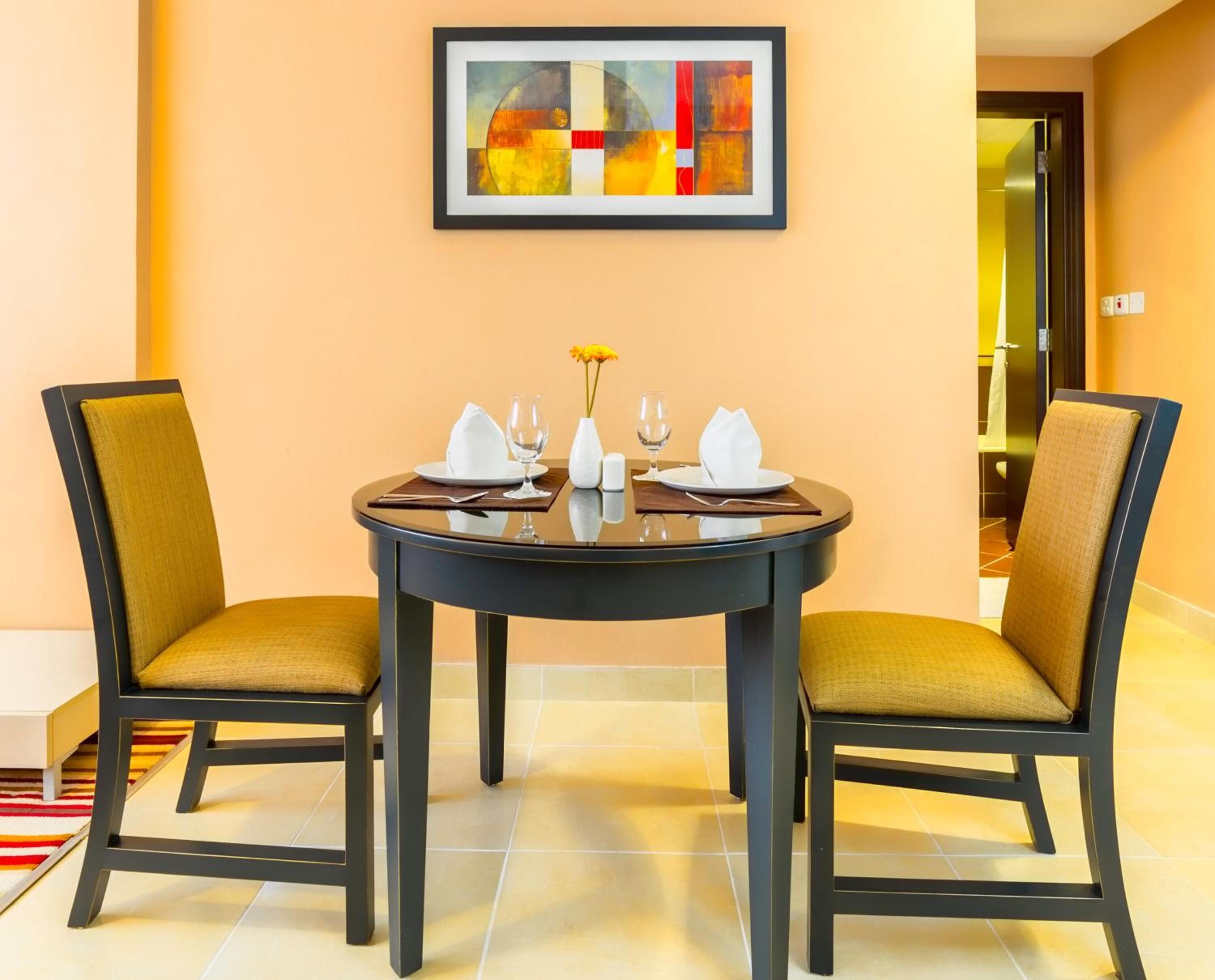 A dining area with a round table, two chairs, and a framed abstract painting on the wall.