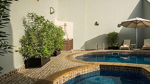 Una piscina con bordes de azulejos, rodeada de sillas de descanso, sombrillas y plantas en macetas.