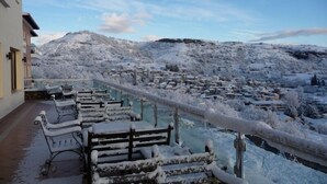 A balcony with snow-covered furniture and a view of a snow-covered village and mountains. - Afkos Grammos Luxury Boutique Hotel (Nestorio)