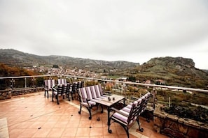 A terrace with outdoor seating and a view of a hilly landscape. - Afkos Grammos Luxury Boutique Hotel (Nestorio)