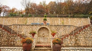 A stone wall with a small arched entrance, flanked by two large planters with flowers. - Afkos Grammos Luxury Boutique Hotel (Nestorio)