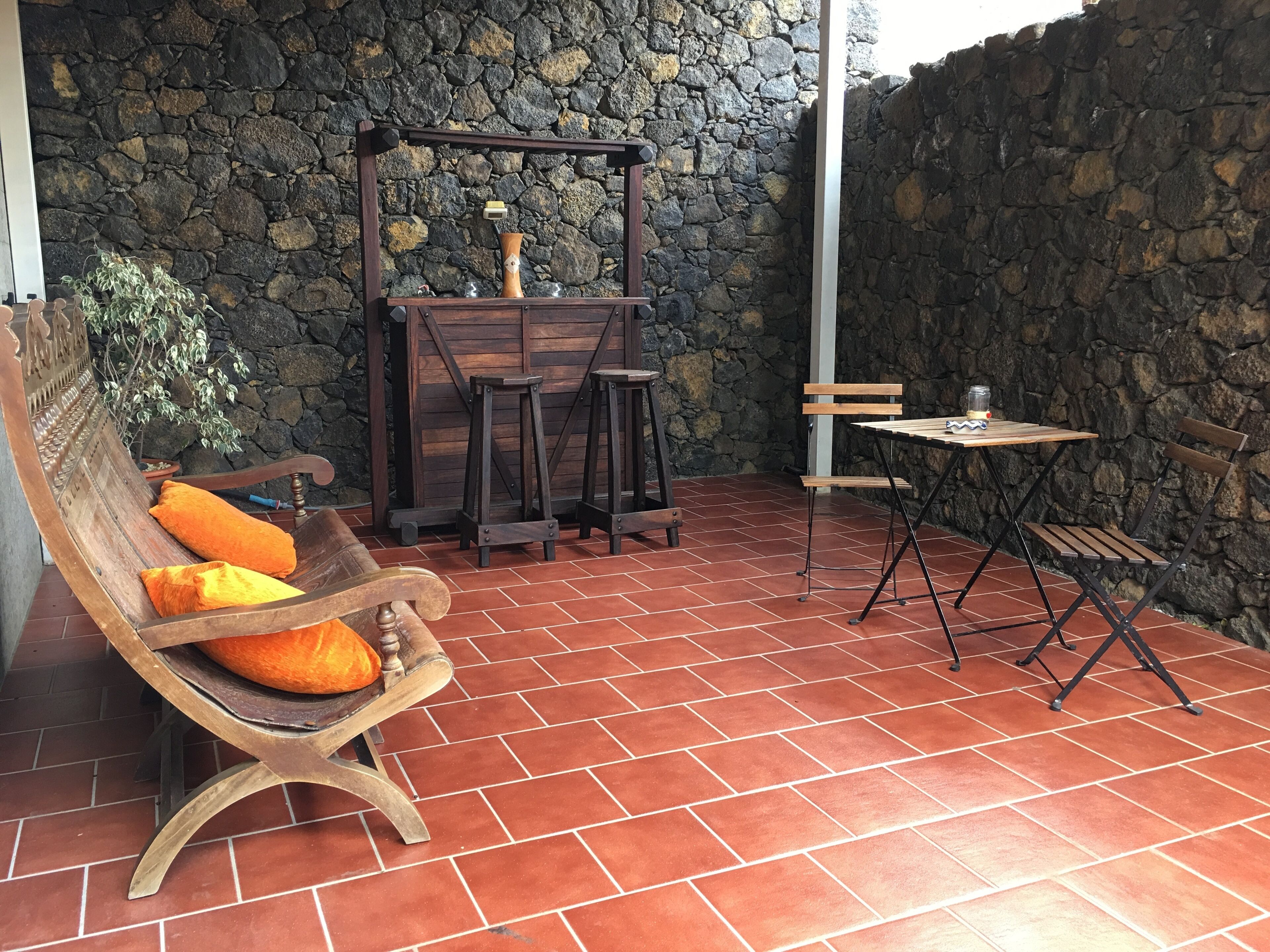 A patio with a wooden bench, two stools, and a small table.
