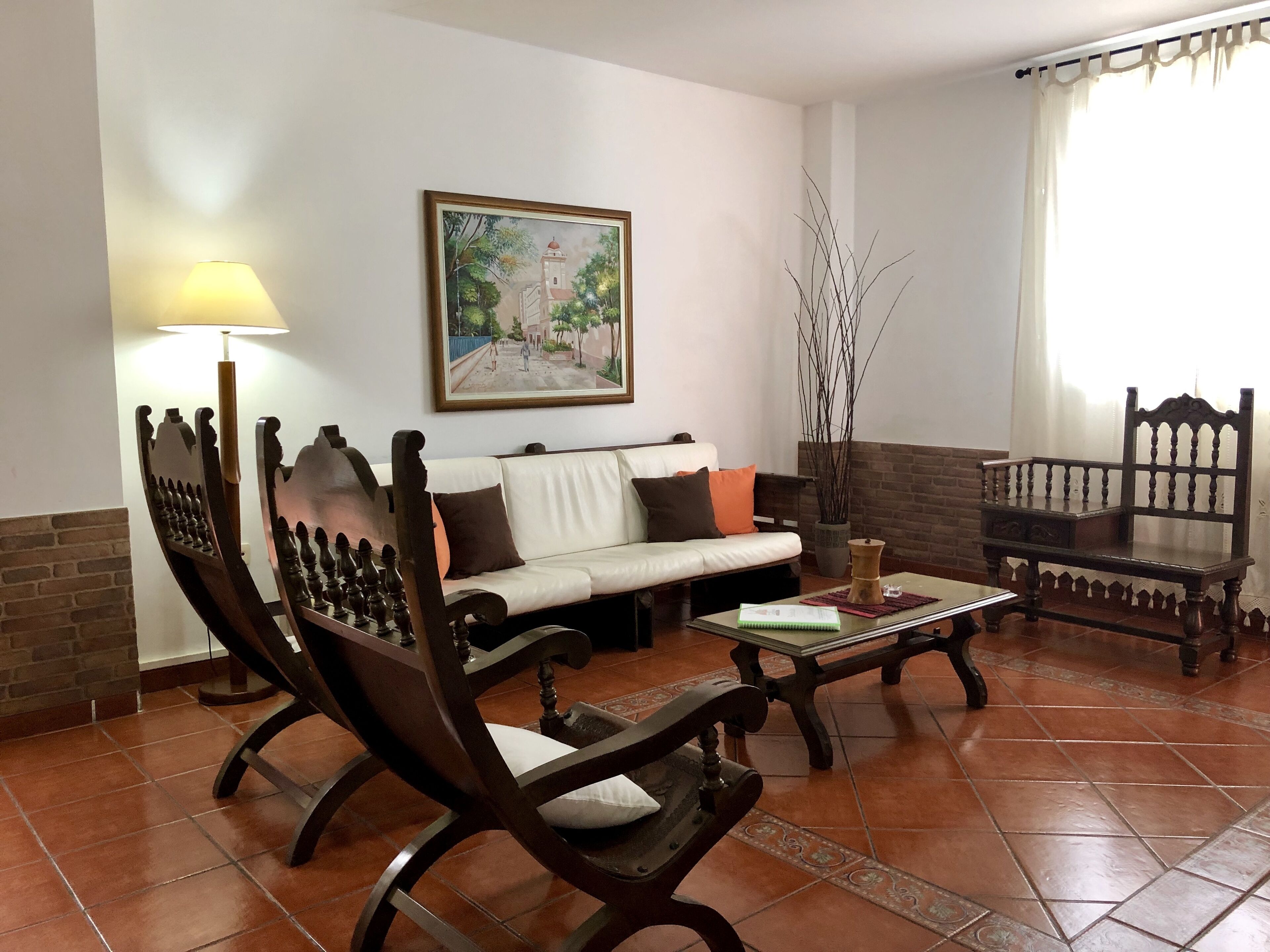Un salón con sofá, dos sillas de madera, una mesa de centro, una lámpara, un cuadro y una planta en maceta.