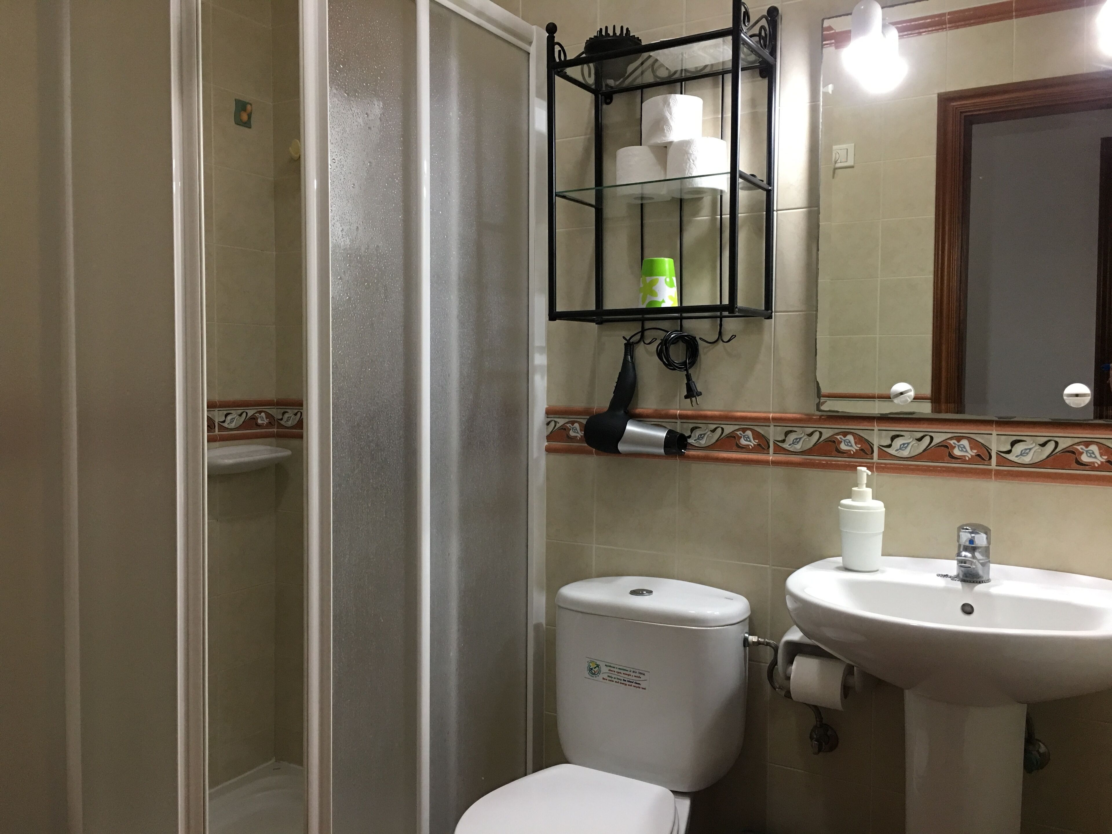 A bathroom with a toilet, sink, and a glass shelf with toiletries.