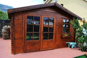 A wooden cabin with large windows, a small wheelbarrow, and a planter box. - Apartamentos Los Verodes (Frontera)