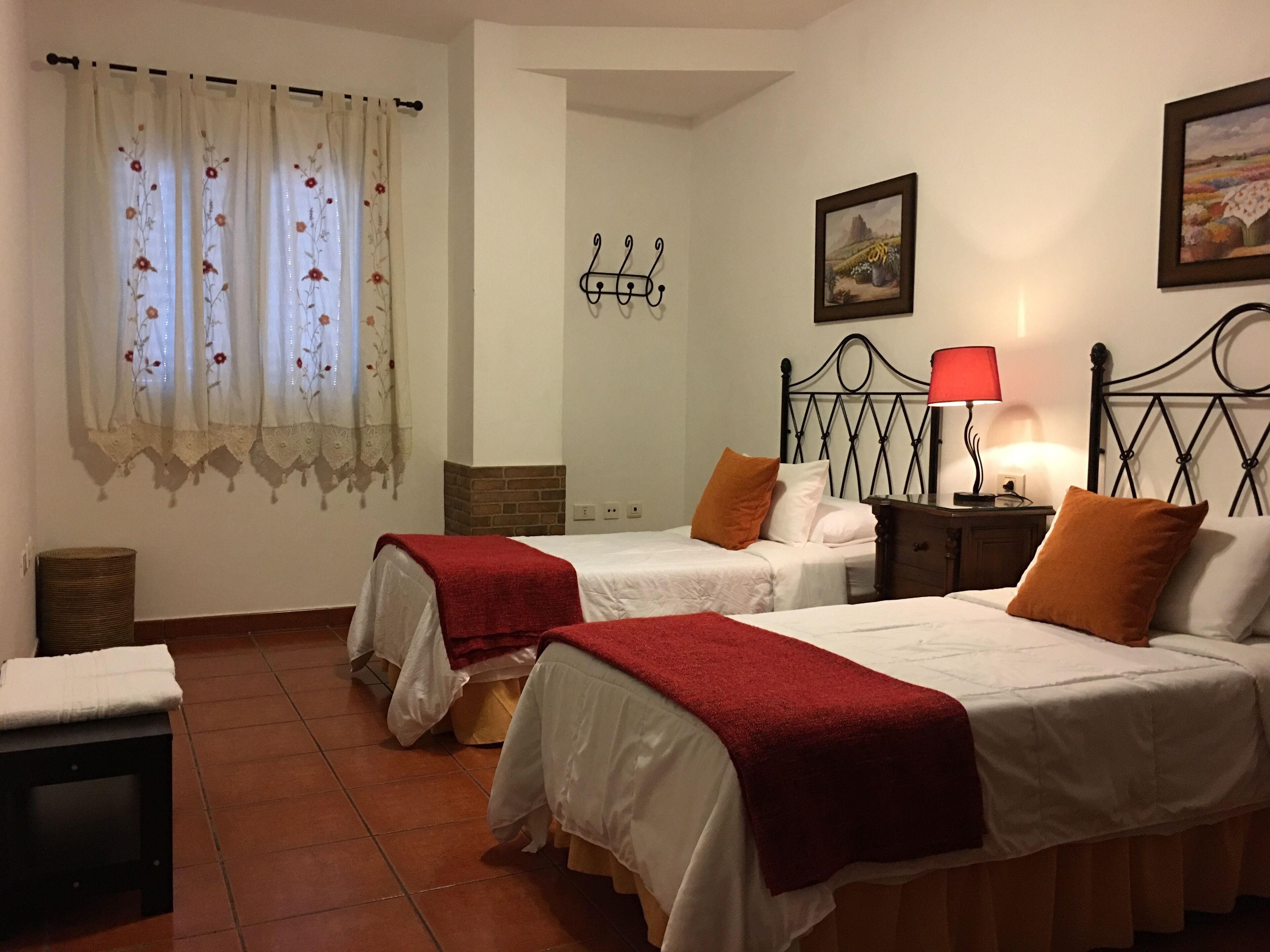 Habitación de hotel con dos camas, una mesita de noche con lámpara, perchero en la pared y un cuadro.