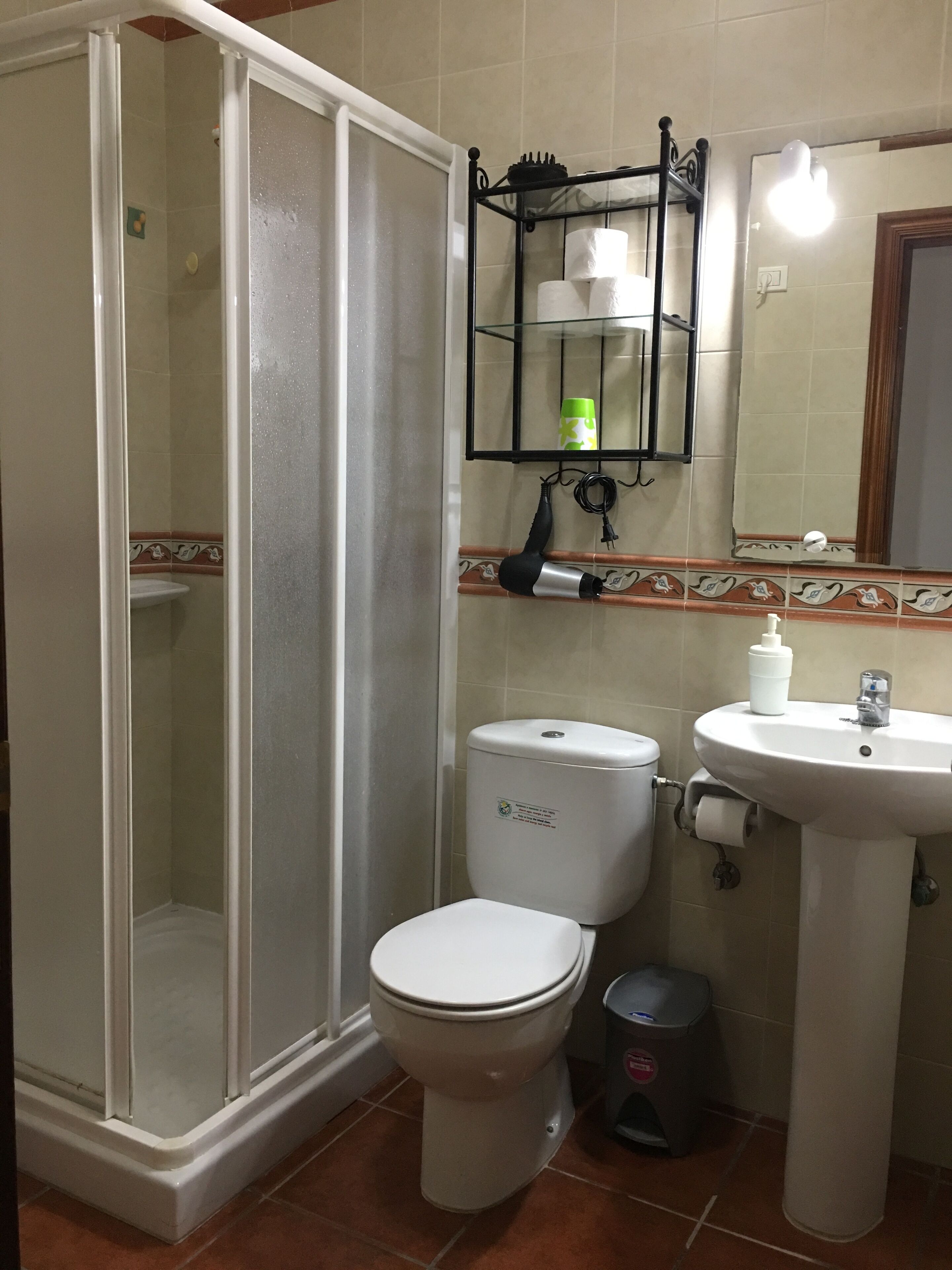 Une salle de bain équipée d’une douche, de toilettes, d’un lavabo et d’une étagère où sont rangés les articles de toilette.