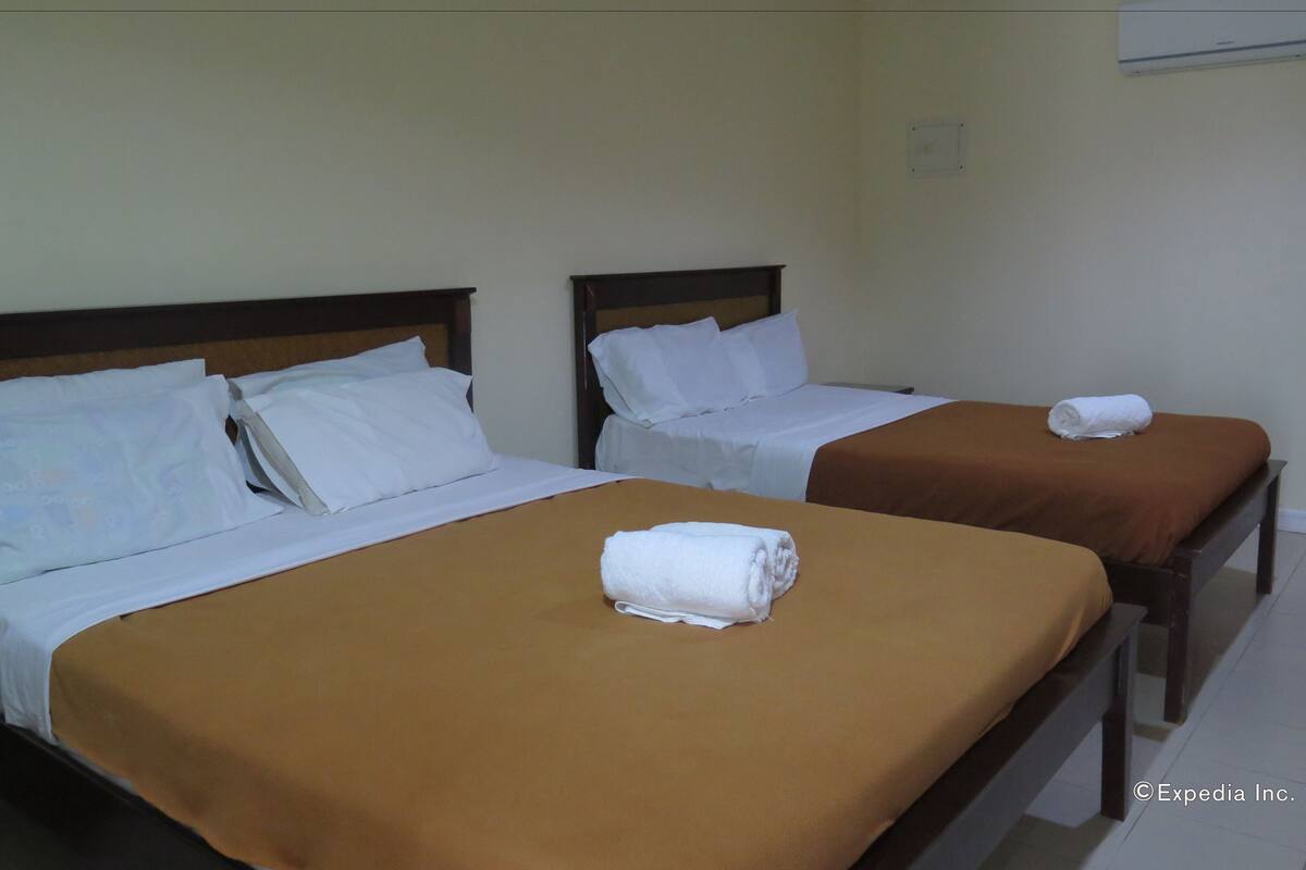 Two single beds with brown and white bedding, a rolled towel on the bed, and a wall-mounted air conditioner.