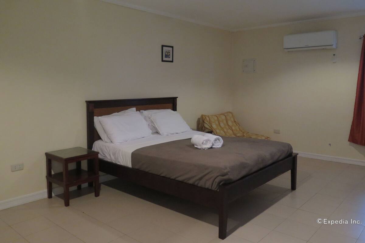 A bedroom with a bed, a nightstand, an air conditioning unit, and a ceiling fan.