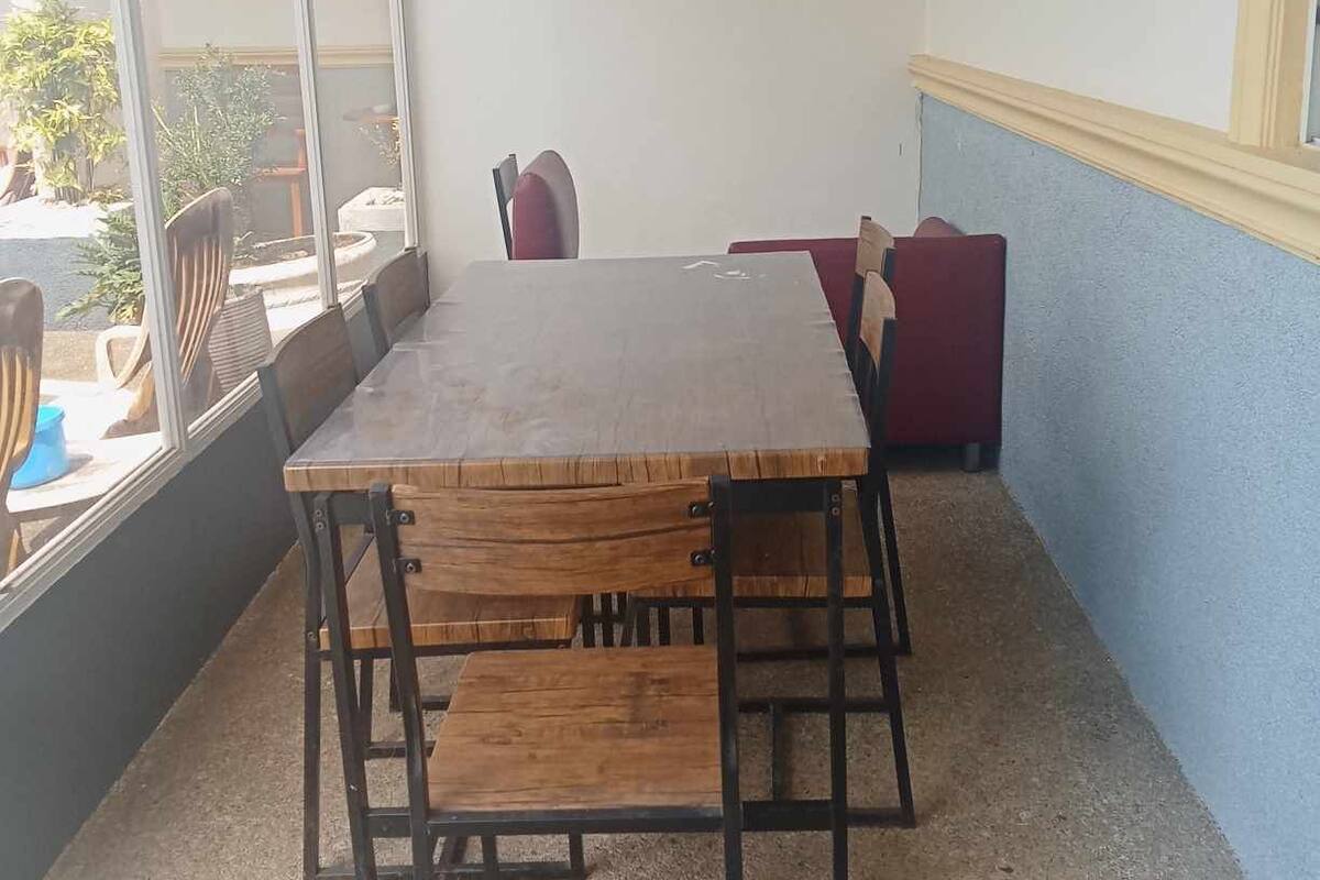 A room with a large wooden table and chairs, a window with a view of the outside, and a small window on the wall.