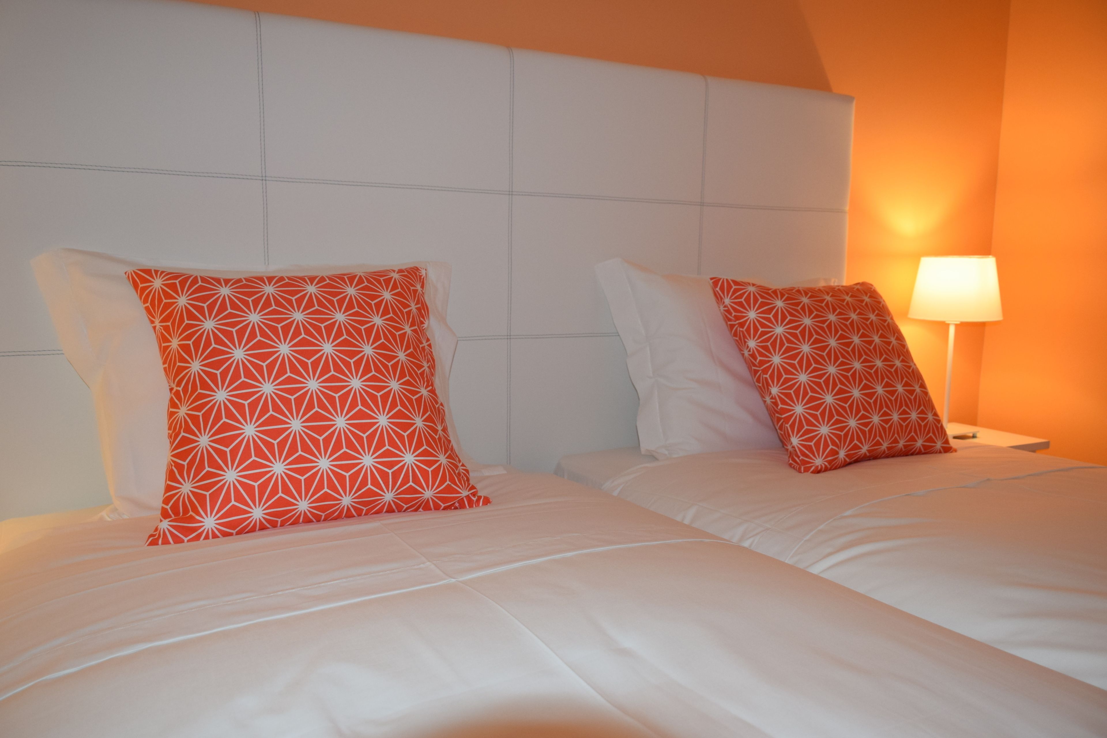 A hotel room with two beds, each with white bedding and orange patterned pillows.