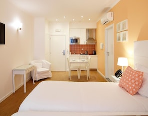 A hotel room with a bed, a desk, a chair, a small table, a kitchenette, and a phone on the bedside table. - Rossio Apartments (Lisbon)