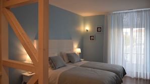Un dormitorio con dos camas, una mesita de noche, una lámpara y una ventana con cortinas translúcidas.
