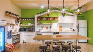 A modern kitchen with a wooden table and bar stools, green walls, white cabinets, and various kitchen appliances. - Green Hotel - Fengjia (Taichung)