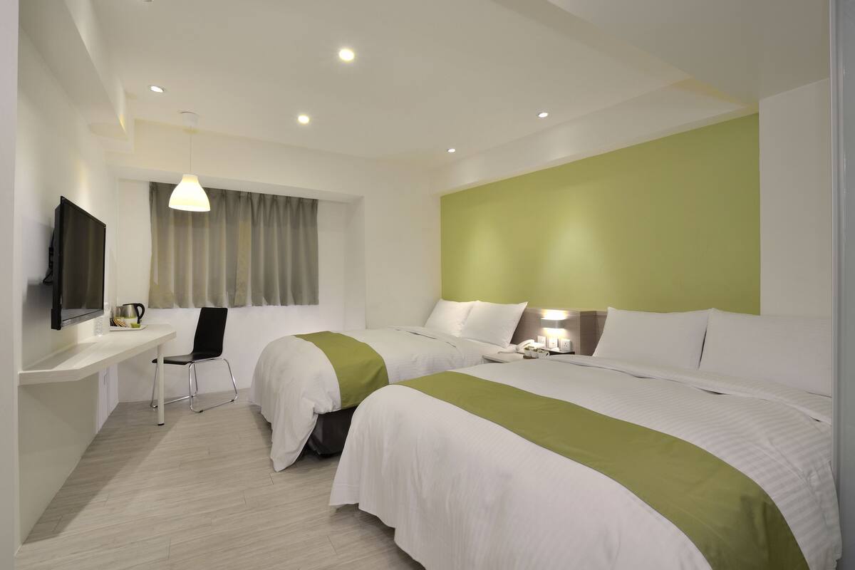 A hotel room with two beds, a desk with a chair, a television, and a window with curtains.