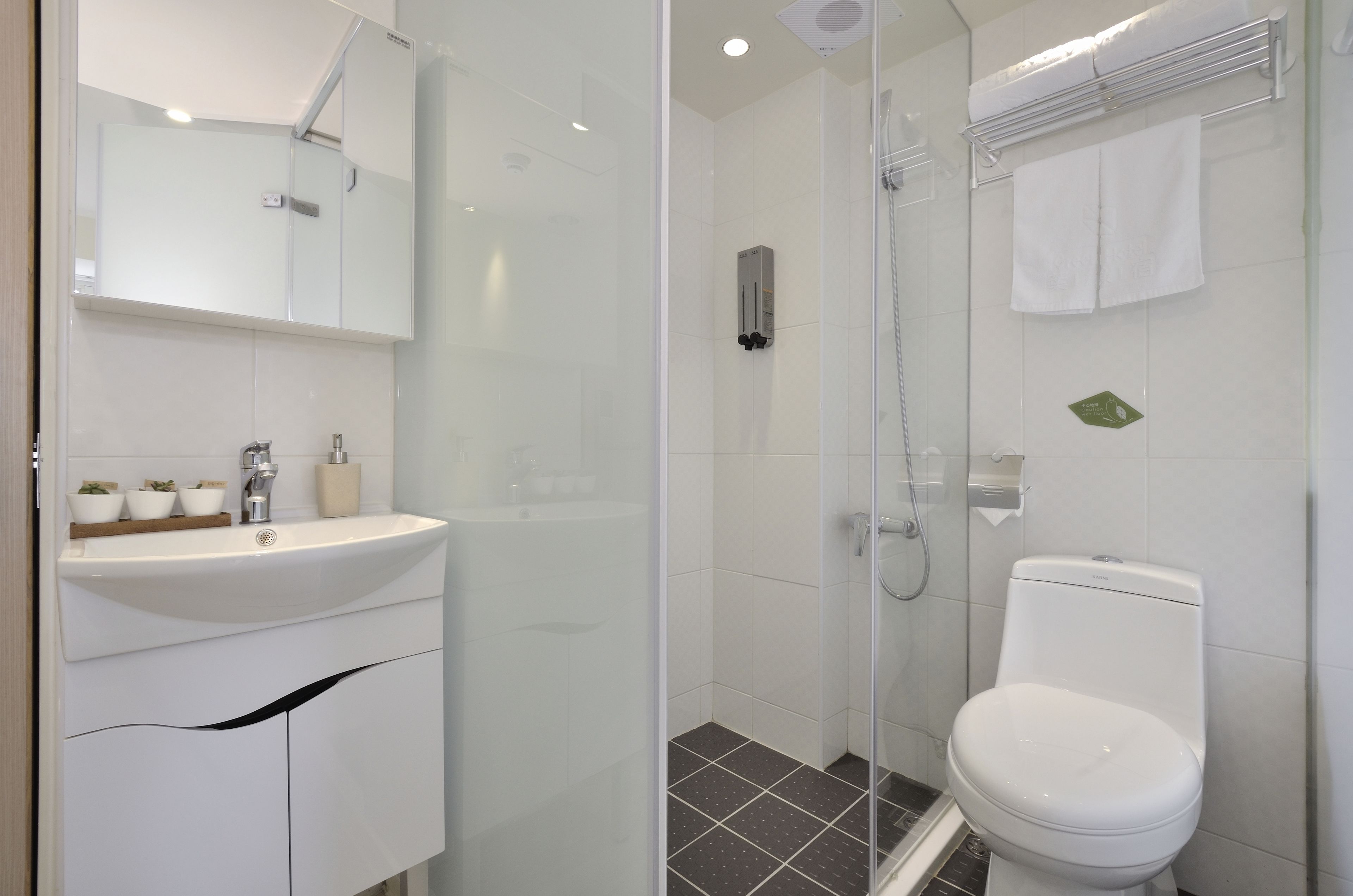 Un baño moderno con cabina de ducha de vidrio, un lavabo blanco con espejo y un inodoro con toallero.