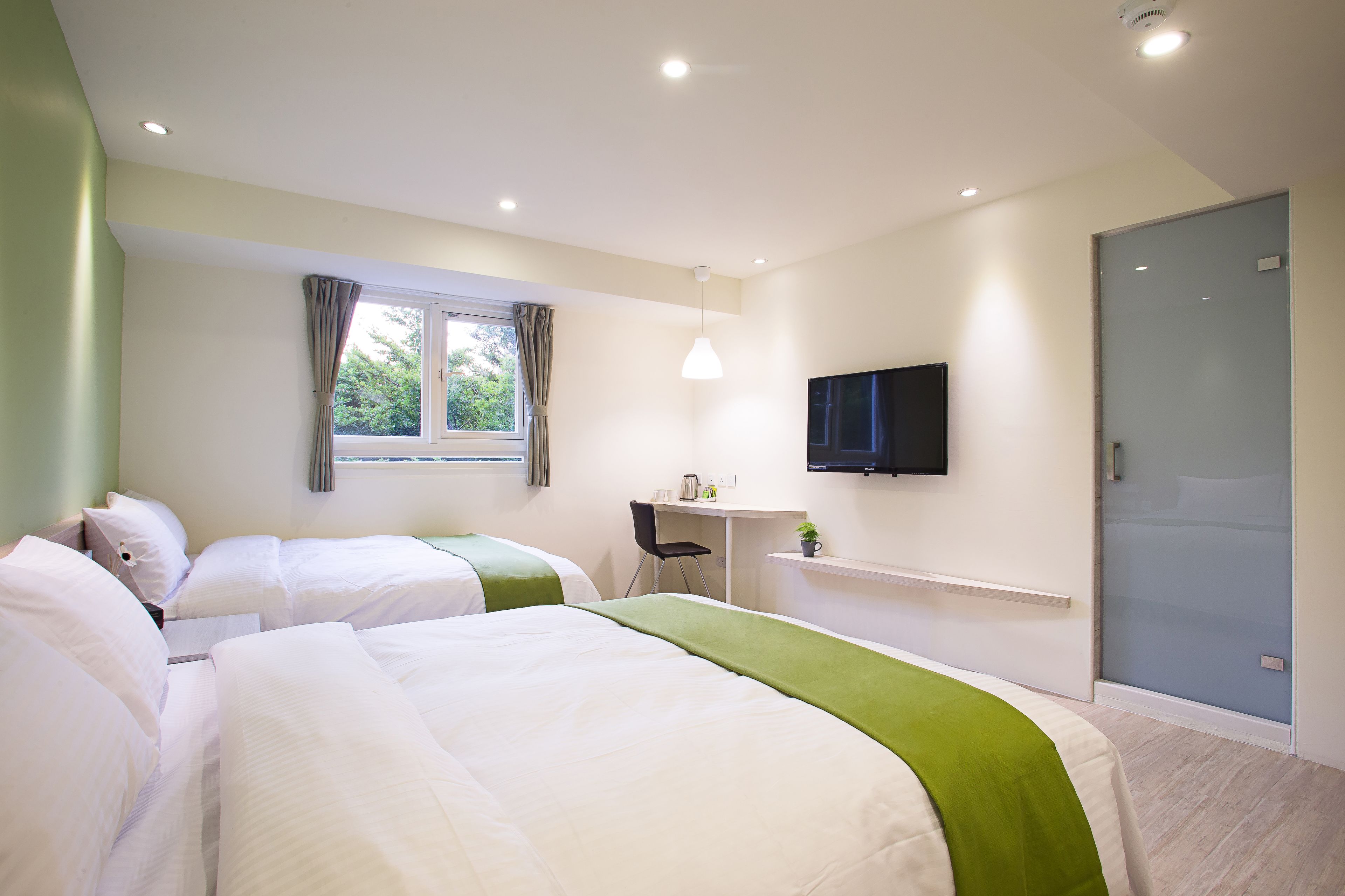 A hotel room with two beds, a desk, a television, and a window with curtains.