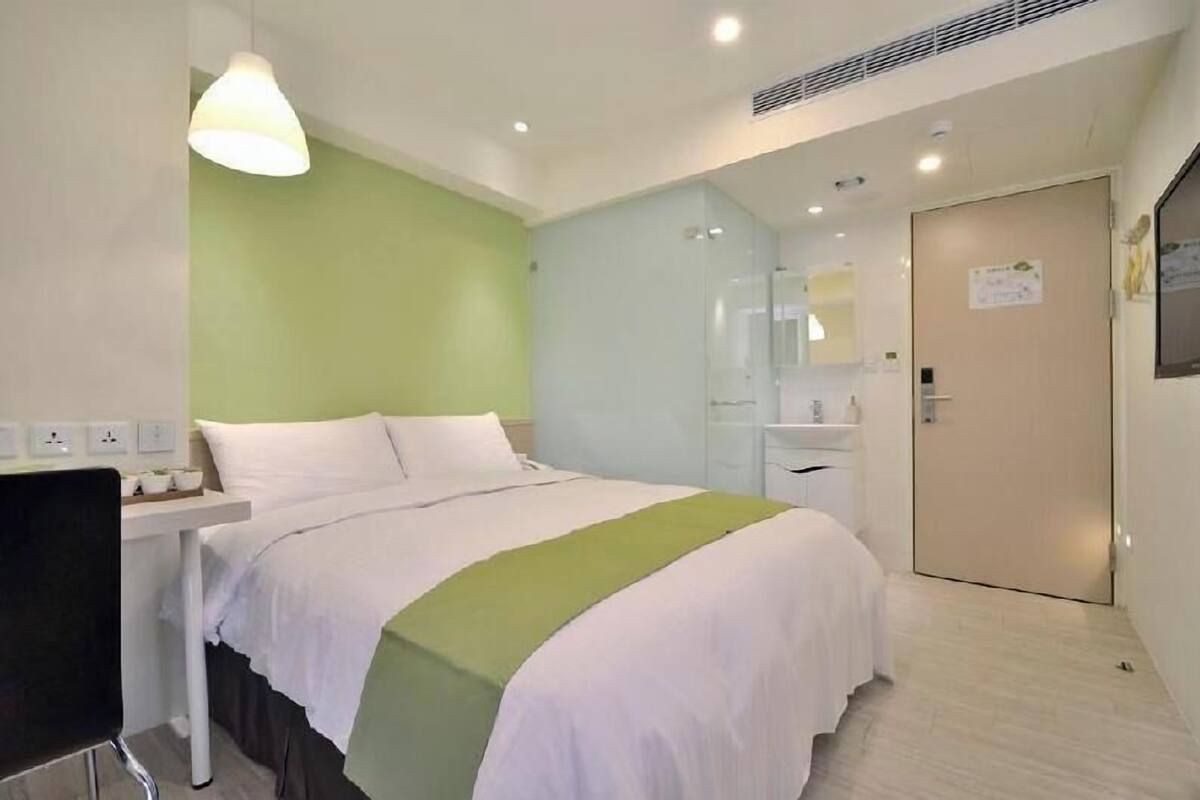 A hotel room with a bed, bedside table, lamp, and a door with a sign.