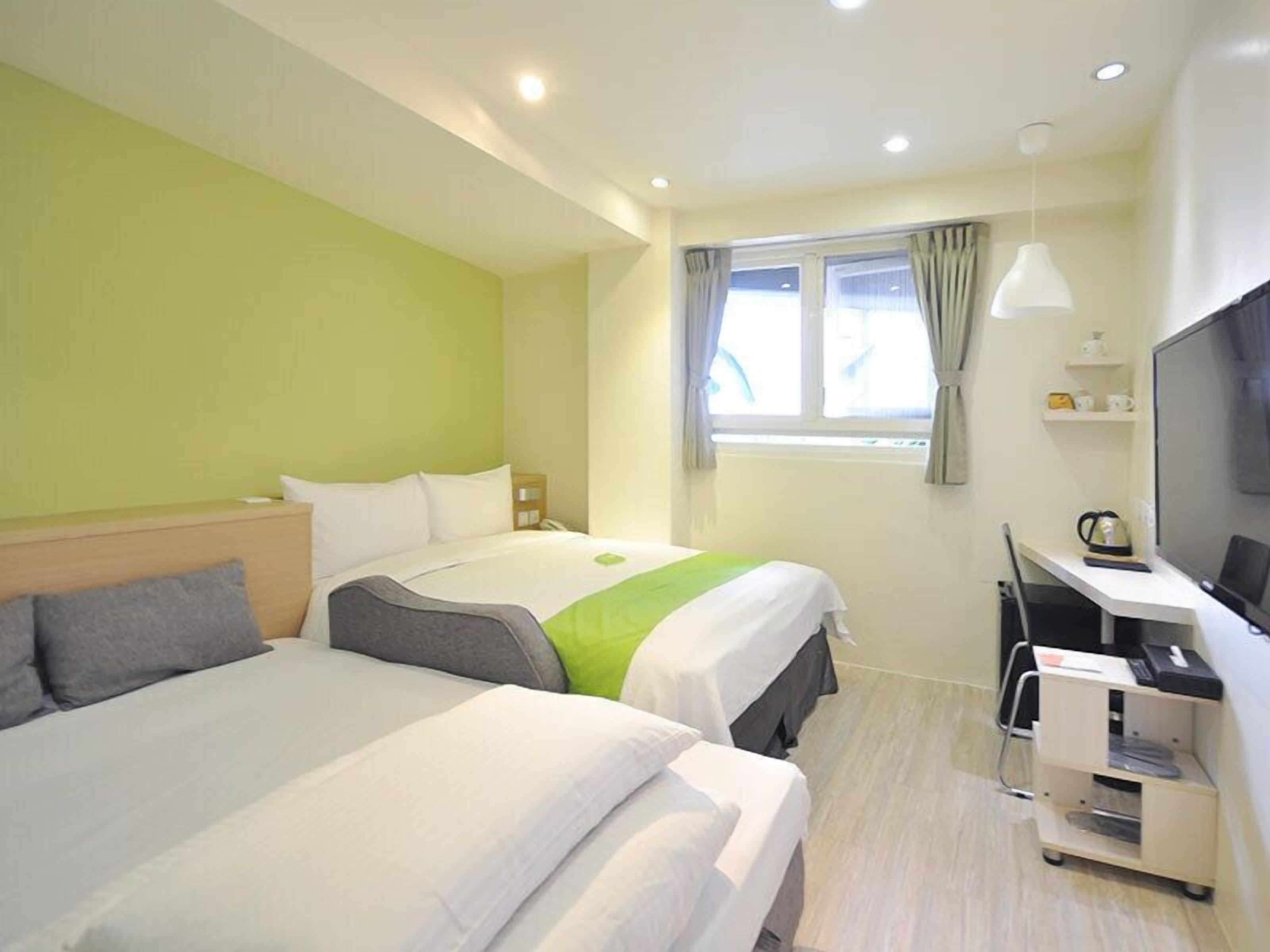 A hotel room with two beds, a desk with a chair, a television, and a window with curtains.