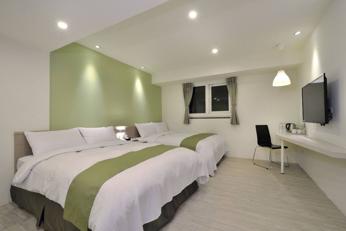A hotel room with two beds, a desk, a chair, a TV, and a window with curtains.
