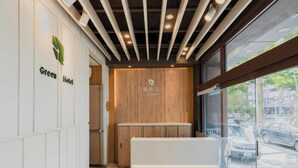 A reception area with a wooden panel wall, a reception desk, and a window with a view of the street. - Green Hotel - Fengjia (Taichung)