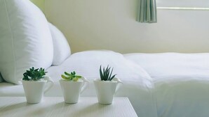 A neatly made bed with white bedding, three small potted plants on a white table, and a window with a curtain. - Green Hotel - Fengjia (Taichung)