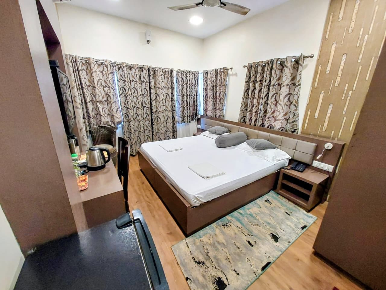 A hotel room with a bed, a desk, a chair, a small table, and a ceiling fan.