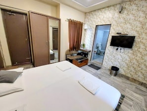 Quarto de hotel com uma cama grande, guarda-roupa, escrivaninha com cadeira, televisão e espelho.
