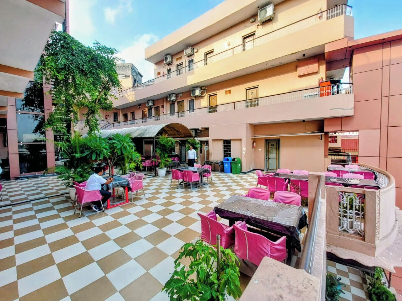 A courtyard with checkered flooring, outdoor seating with pink chairs, and a building with multiple balconies.