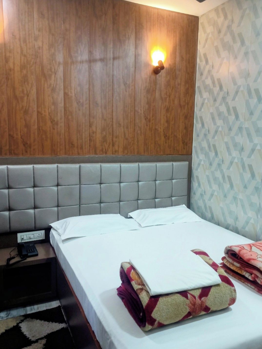 Ein Hotelzimmer mit einem hölzernen Kopfteil, einem Bett mit weißer Bettwäsche, einem Nachttischtelefon und einer Wand mit Muster.