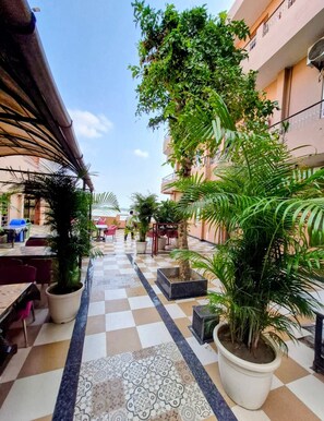 A courtyard with a checkered floor, potted plants, outdoor seating, and a building with balconies. - Hotel Alka (Varanasi)