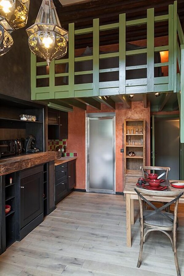 A kitchen with a wooden countertop, a stainless steel refrigerator, and a dining area with a wooden table and chairs.