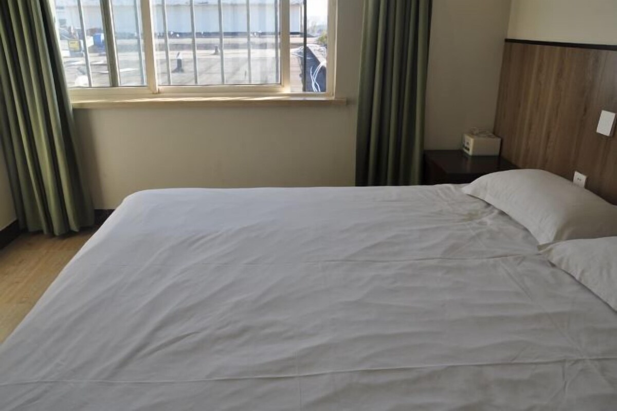 A hotel room with a large bed, a nightstand, a lamp, and a window with curtains.