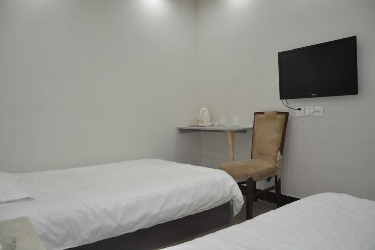 A room with two beds, a chair, a small table, and a mounted TV.