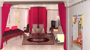 A living room with a bed, a sofa, a TV, and a decorative wall. - Bhanwar Vilas Guest House (Udaipur)